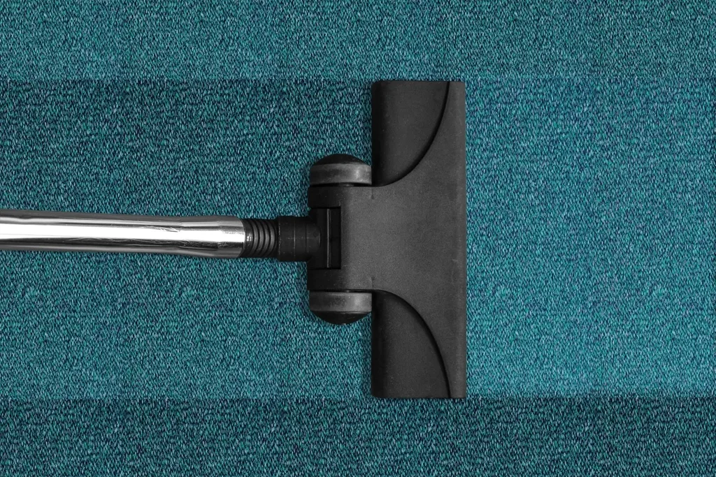 La brosse d’un aspirateur posée sur une moquette bleu canard