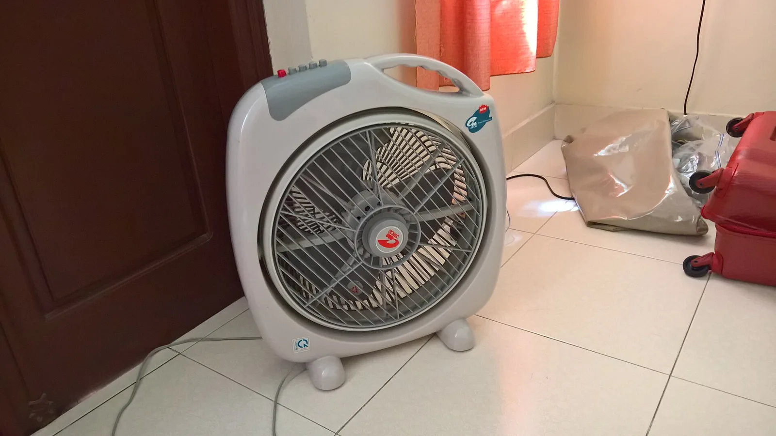 Un ventilateur posé au sol, tourné vers la pièce, près d’une fenêtre