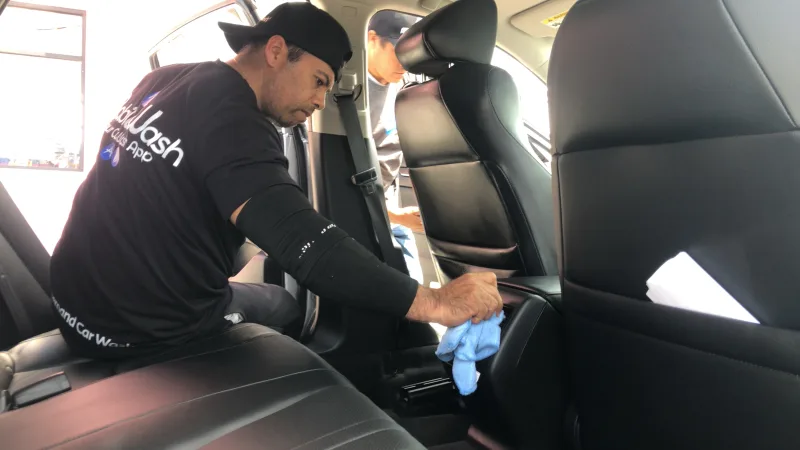 Un homme nettoie au chiffon l’intérieur d’une voiture, penché sur la banquette arrière